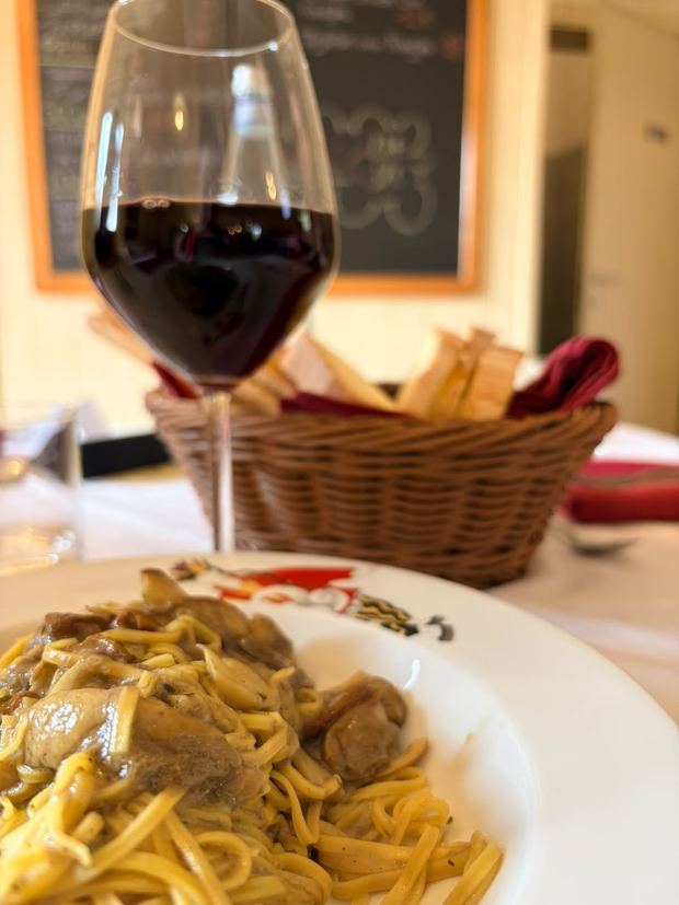 Tajarin ai funghi e un calice di rosso, con la lavagna del menù sullo sfondo